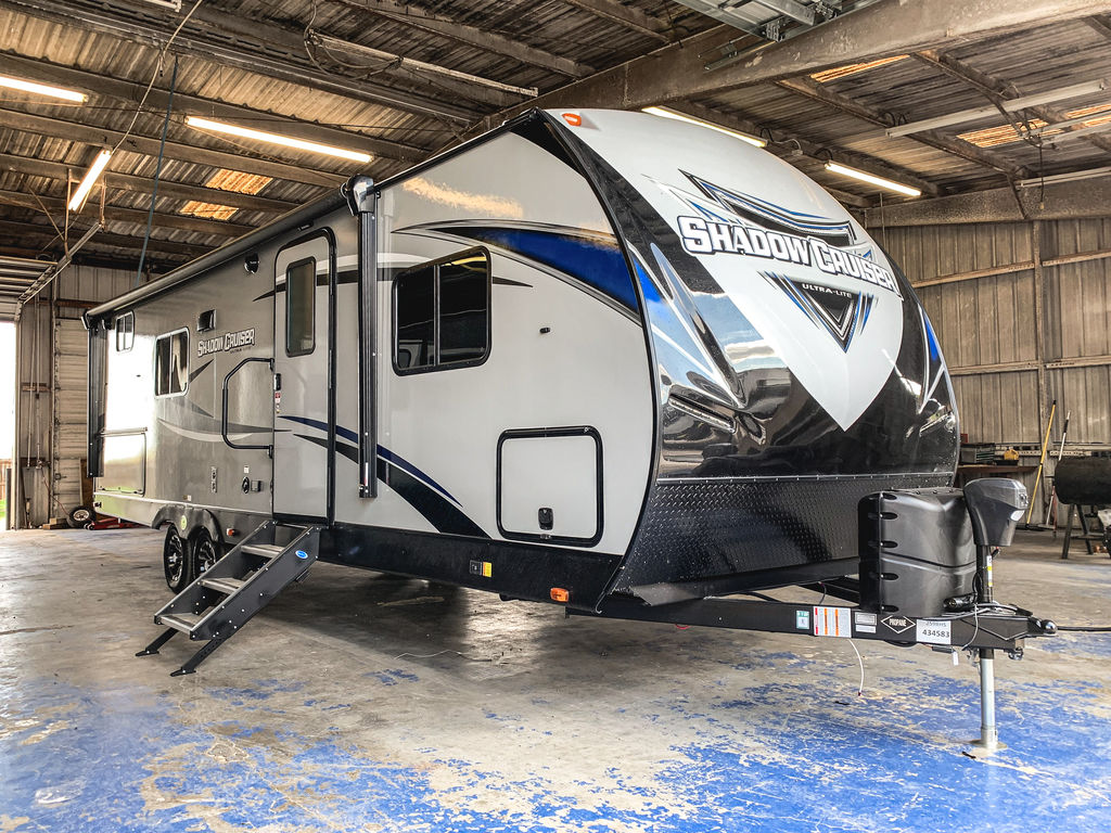 A white & grey 2020 Cruiser RV Shadow Cruiser bunkhouse RV parked inside a garage with its staircase open.